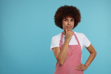 Photo of Thoughtful young woman in apron on light blue background. Space for text