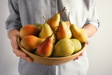 Woman holding bowl with ripe pears on light background, closeup