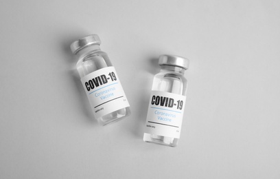 Vials with coronavirus vaccine on light background, flat lay