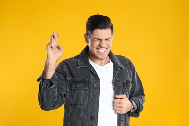 Photo of Man with crossed fingers on yellow background. Superstition concept