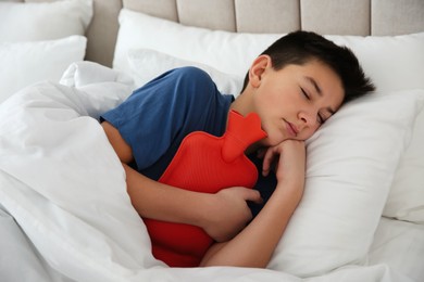 Photo of Sick teenage boy with hot water bottle sleeping in bed at home