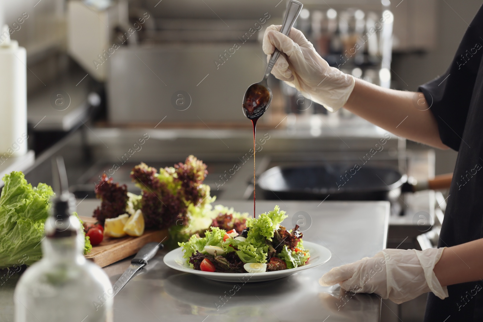 Photo of Female chef adding sauce to cooking food in restaurant kitchen, closeup