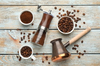 Manual coffee grinder, jezve, powder and beans on wooden table, flat lay