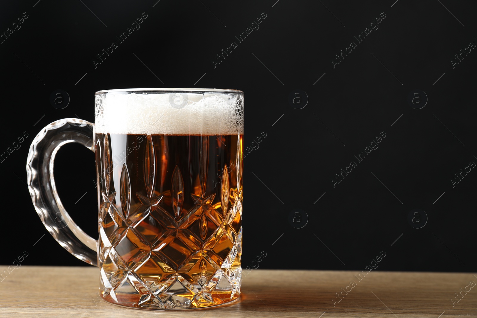 Photo of Mug with fresh beer on wooden table against black background. Space for text