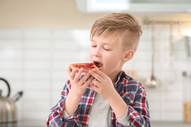 Cute little boy eating tasty toasted bread with jam in kitchen