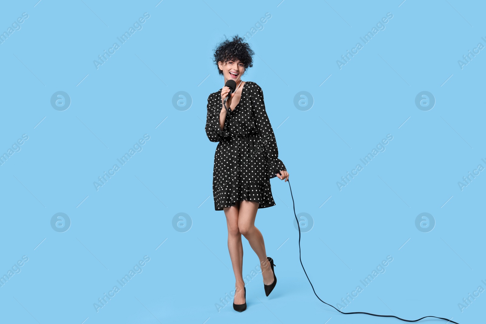 Photo of Beautiful young woman with microphone singing on light blue background