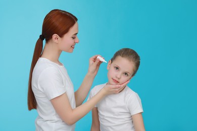 Photo of Mother dripping medication into daughter's ear on light blue background