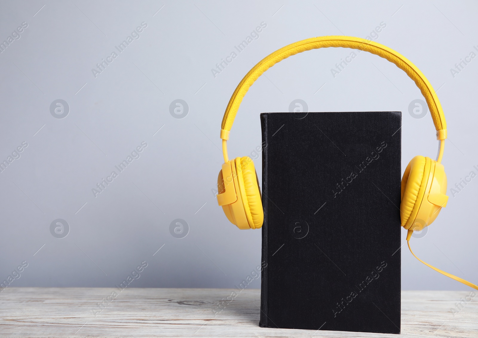 Photo of Book and modern headphones on white wooden table. Space for text
