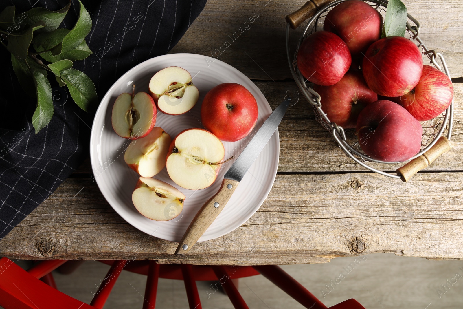 Photo of Fresh red apples, leaves and knife on wooden table, flat lay