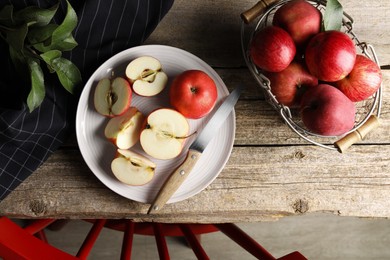 Fresh red apples, leaves and knife on wooden table, flat lay