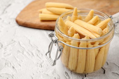 Photo of Jar of pickled baby corn on white textured table, closeup. Space for text