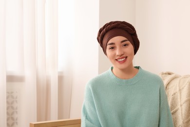 Photo of Cancer patient. Young woman with headscarf near window indoors, space for text