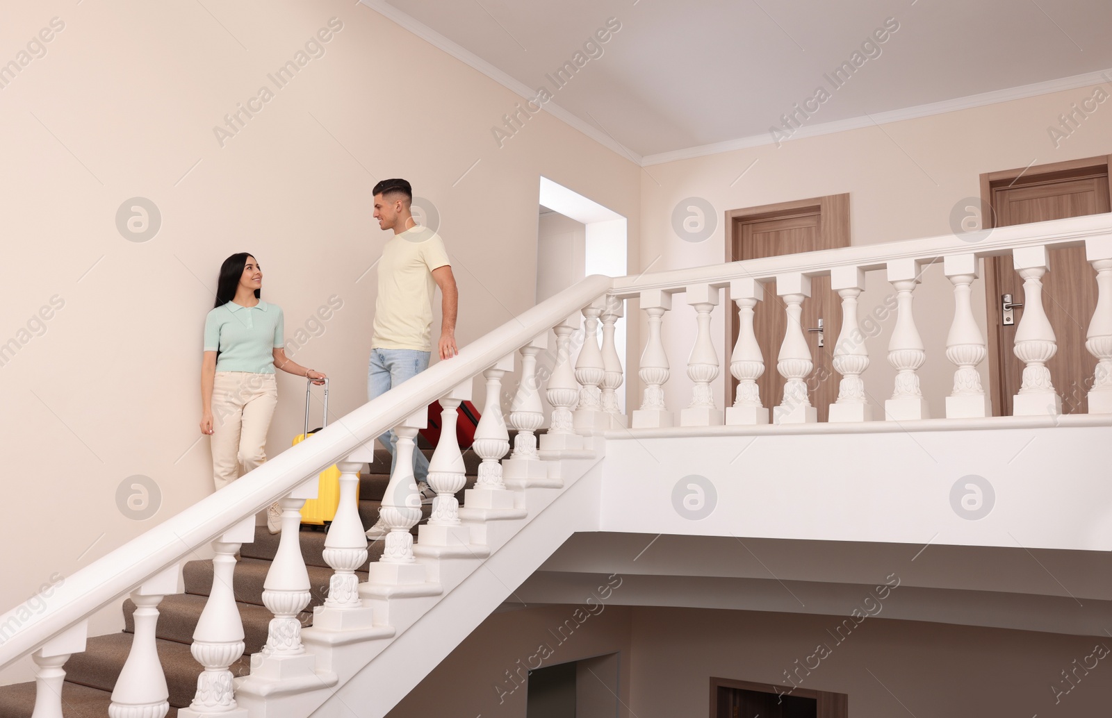 Photo of Happy couple with suitcases going down stairs in hotel