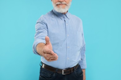 Man welcoming and offering handshake on light blue background, closeup