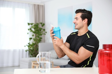 Photo of Young athletic man with protein shake at home, space for text