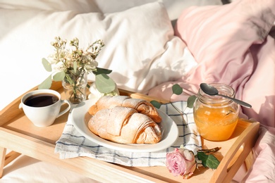 Photo of Tray with delicious croissants, cup of coffee and honey on bed