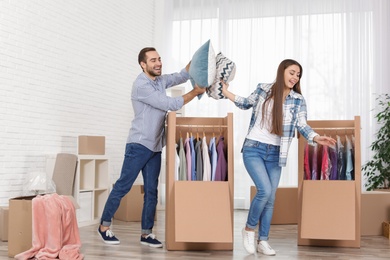 Photo of Young couple having pillow fight near wardrobe boxes at home