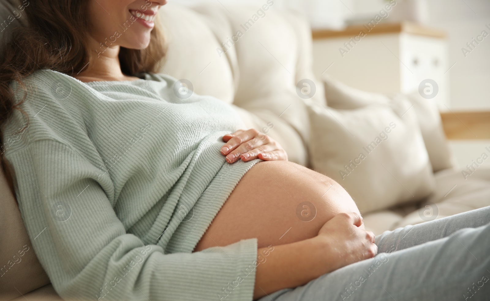 Photo of Pregnant woman touching her belly indoors, closeup