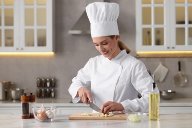 Photo of Professional chef cutting garlic at white marble table indoors