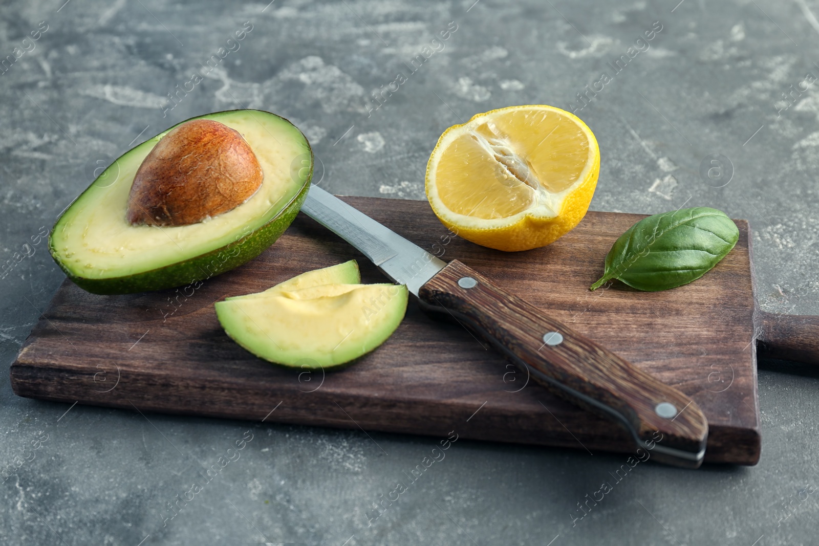 Photo of Wooden board with cut avocado, lemon and knife on grey background