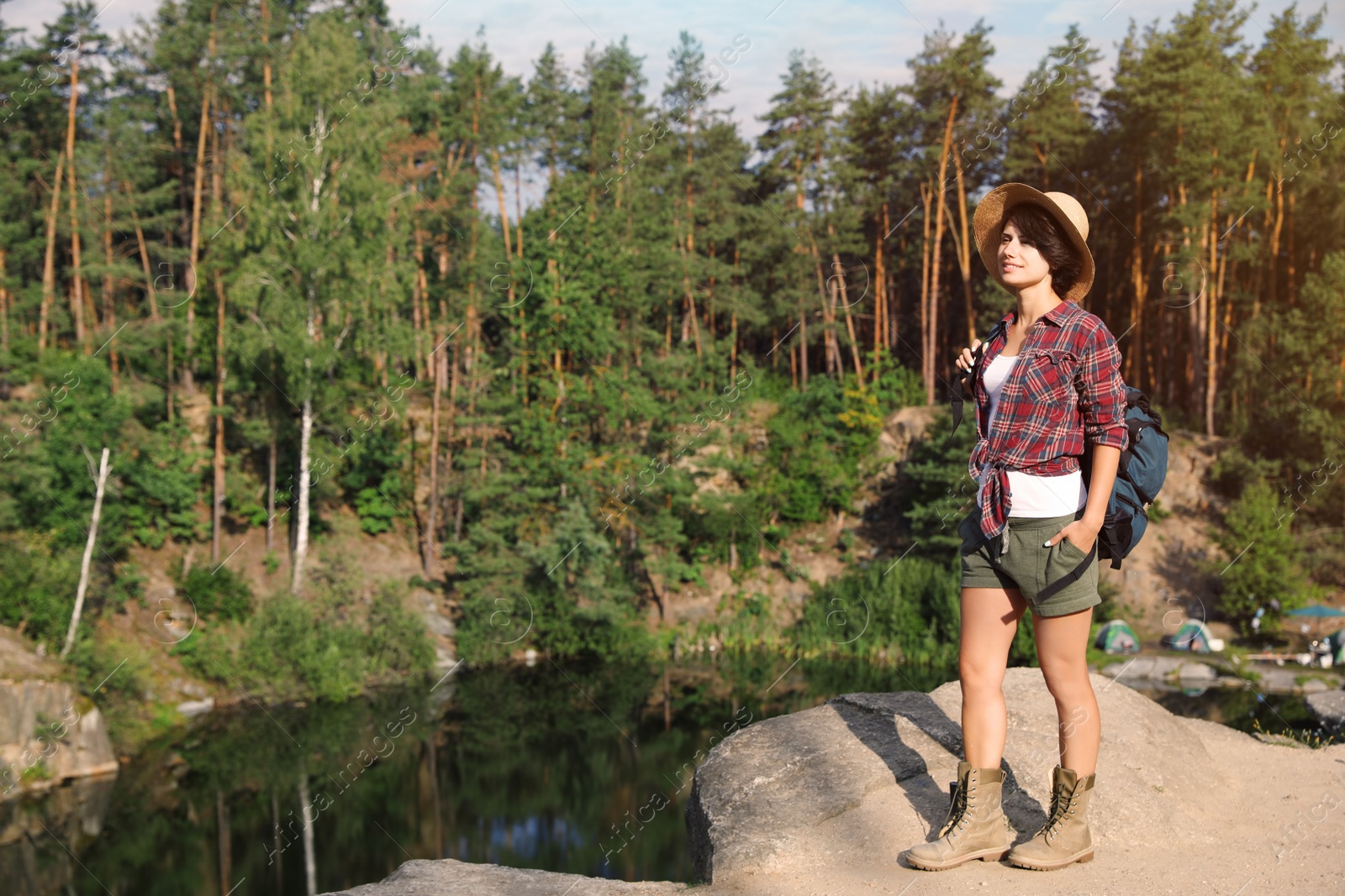 Photo of Young woman on rock near lake and forest. Camping season