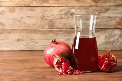 Photo of Jug of pomegranate juice and fresh fruits on table against wooden background, space for text