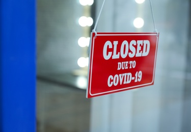 Photo of Red sign with text Closed Due To Covid-19 hanging on glass door, closeup. Coronavirus quarantine