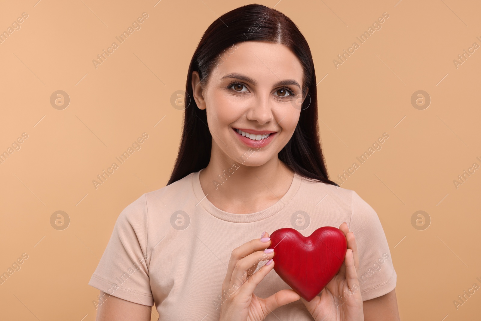 Photo of Happy young woman holding red heart on beige background