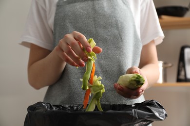 Photo of Woman throwing peels of vegetables into garbage bin in kitchen, closeup