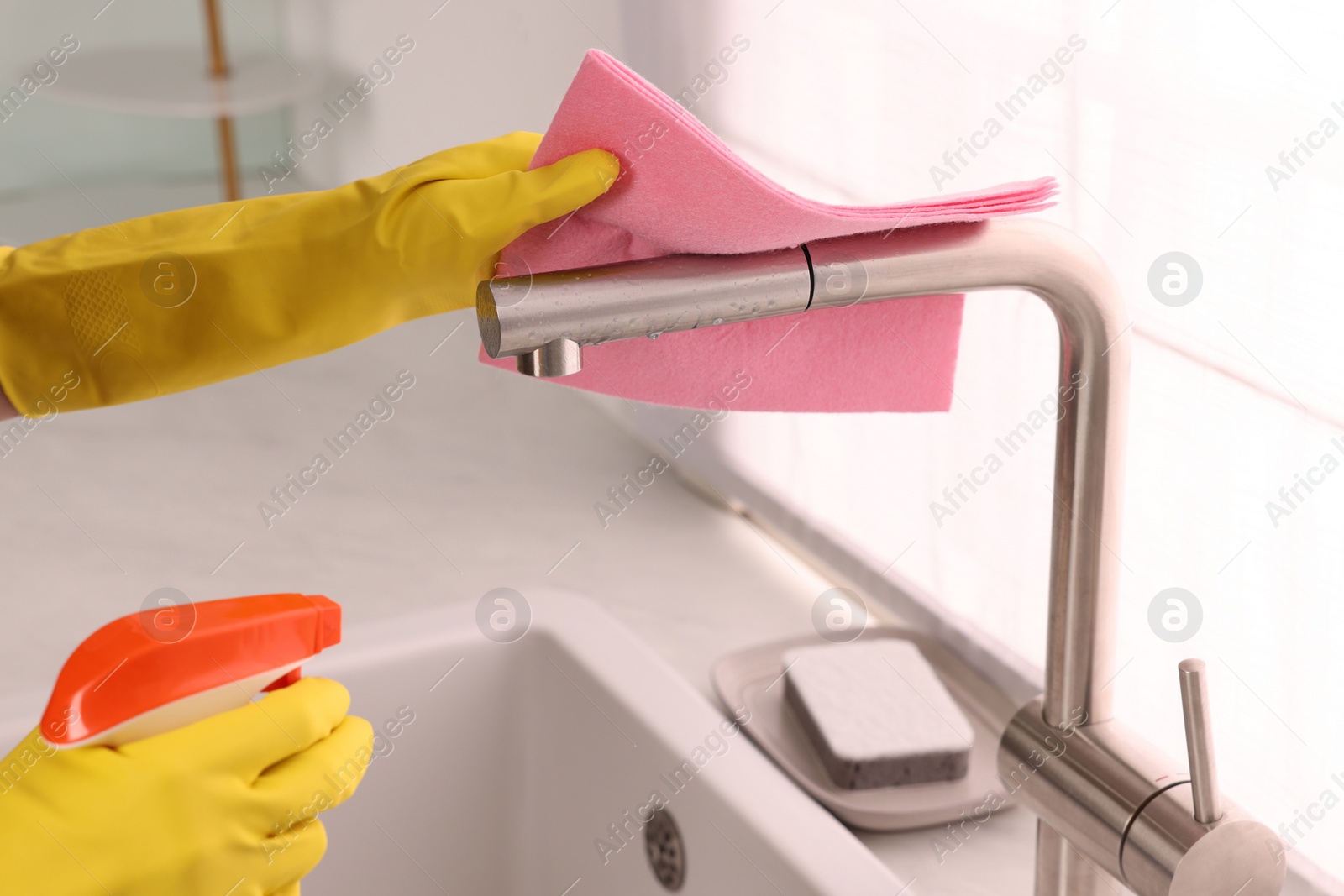 Photo of Woman cleaning faucet with rag and detergent in kitchen, closeup