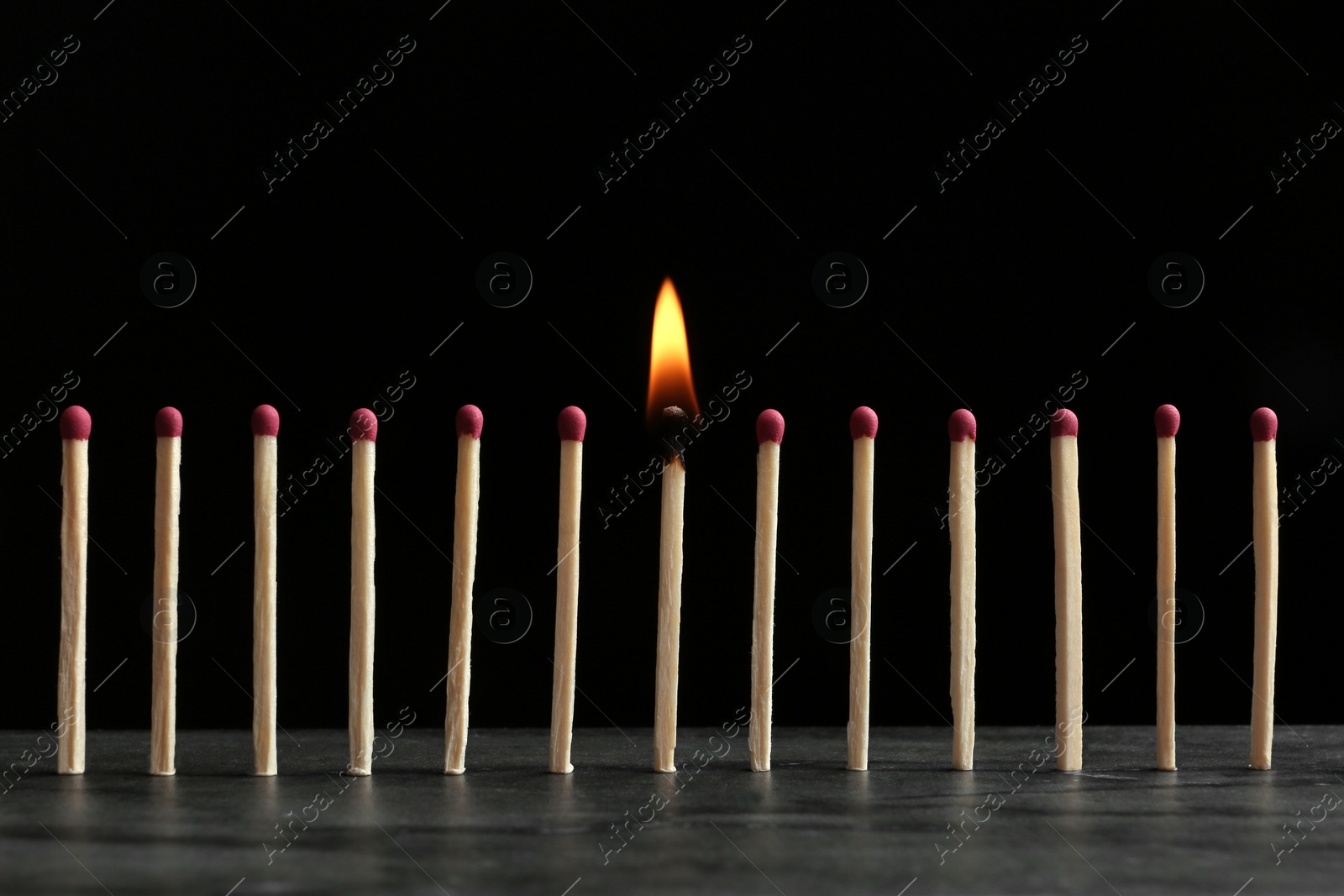 Photo of Burning match among others on table against black background. Difference and uniqueness concept