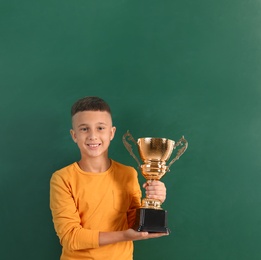 Photo of Happy boy with golden winning cup on near chalkboard