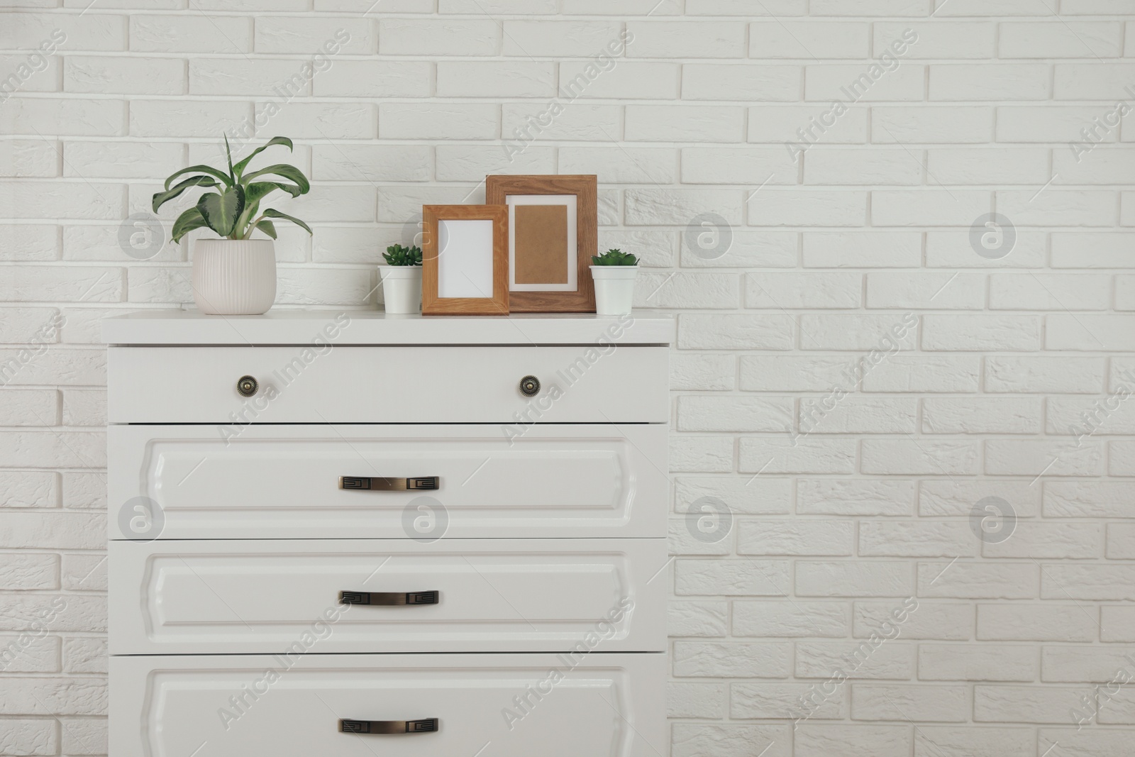 Photo of Modern chest of drawers with decor near white brick wall. Space for text