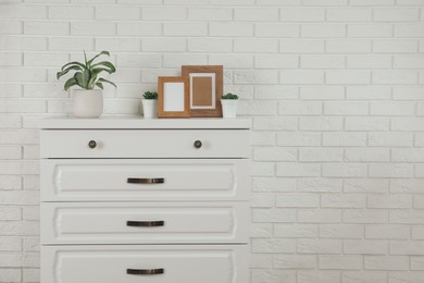 Photo of Modern chest of drawers with decor near white brick wall. Space for text