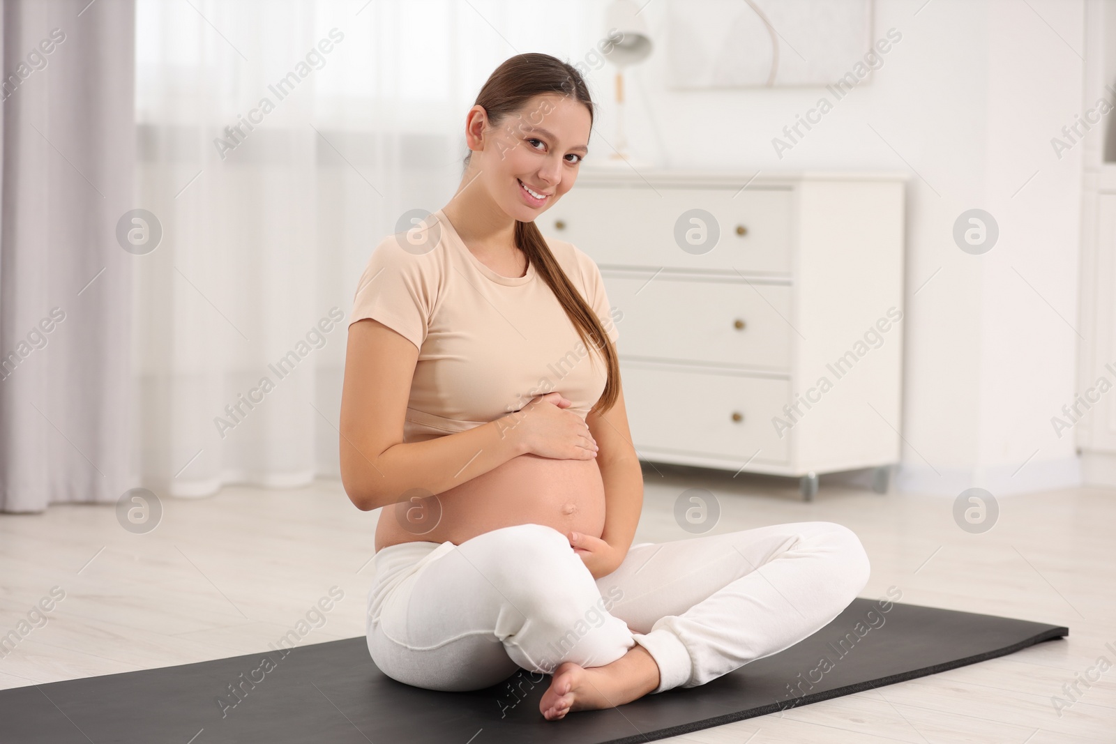 Photo of Pregnant woman sitting on yoga mat at home