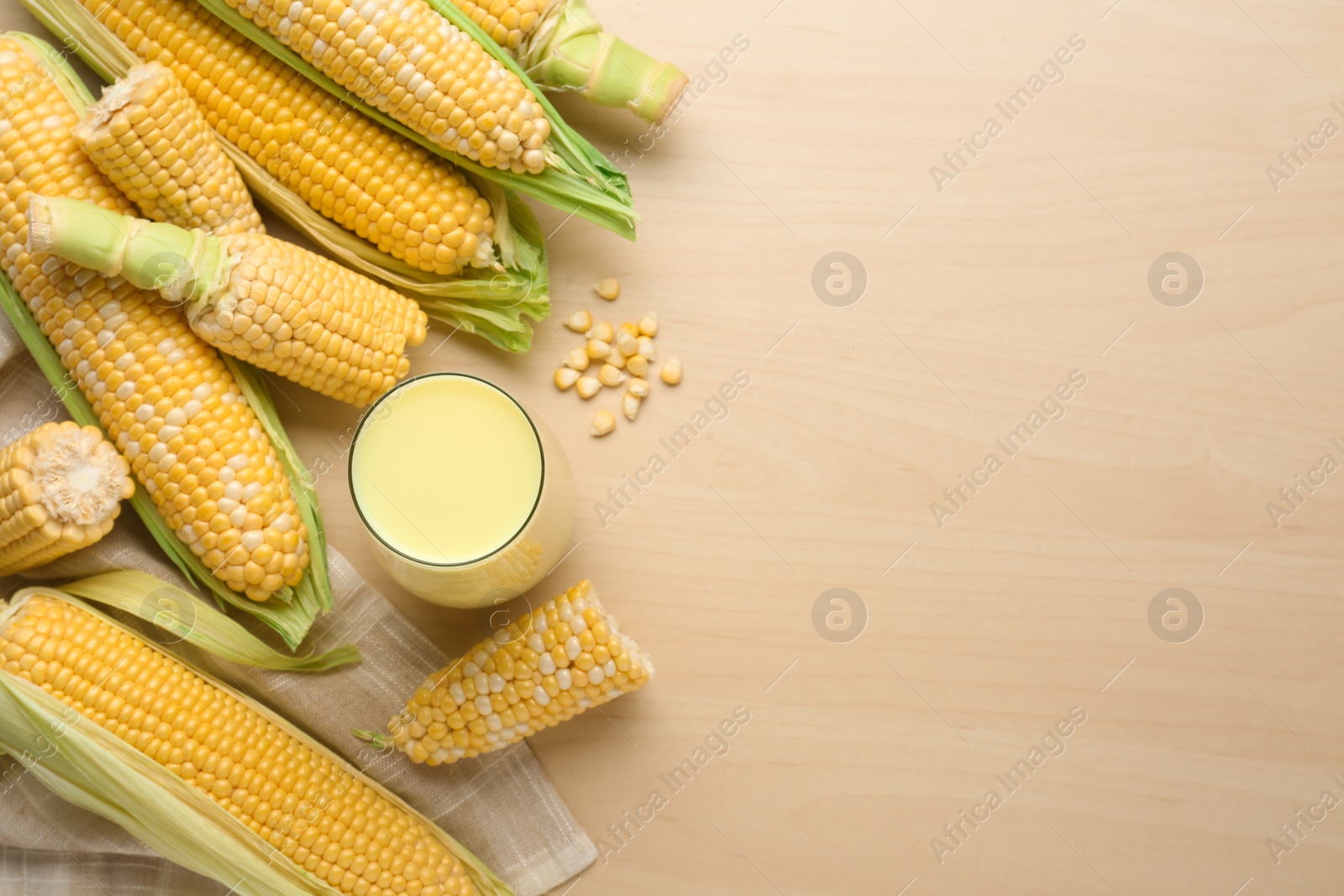 Photo of Corn juice and cobs on wooden table, flat lay. Space for text