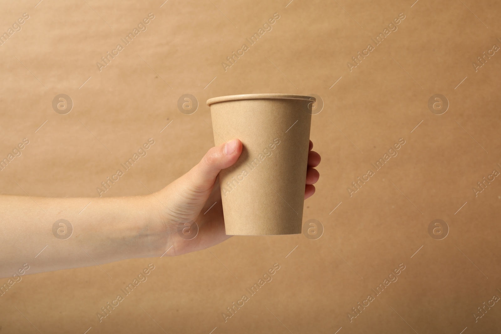 Photo of Woman holding takeaway paper coffee cup on brown background, closeup