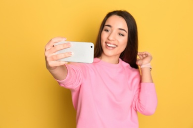 Young beautiful woman taking selfie against color background