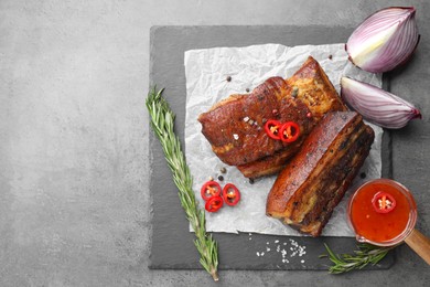 Photo of Pieces of baked pork belly served with sauce, rosemary and chili pepper on grey table, top view. Space for text