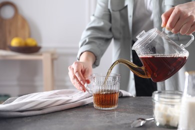 Photo of Woman pouring hot tea into cup at grey table, closeup. Space for text