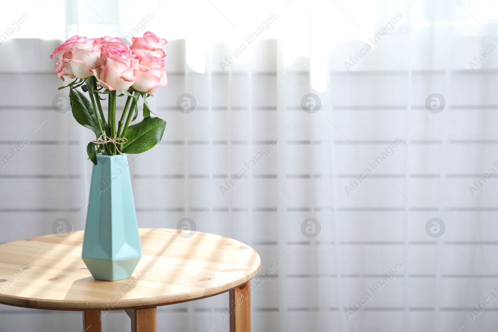 Photo of Vase with beautiful pink roses on wooden table in room. Space for text