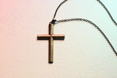 Cross with chain on textured table in color lights, top view. Religion of Christianity