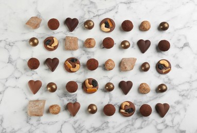 Photo of Different delicious chocolate candies on white marble table, flat lay