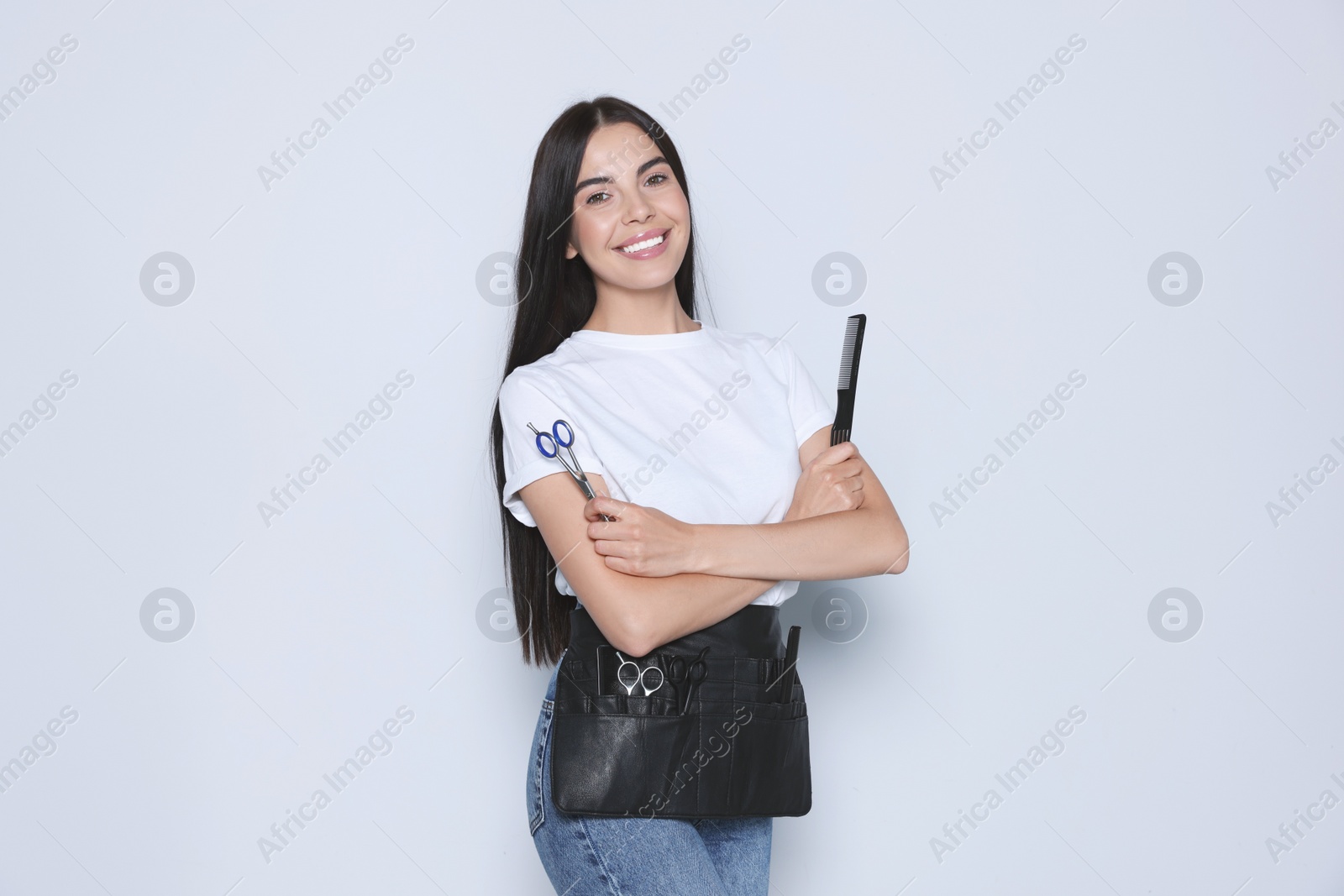 Photo of Portrait of happy hairdresser with professional scissors and comb on light background
