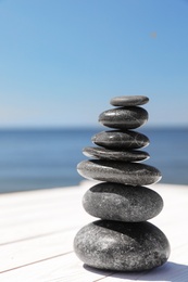 Photo of Stack of stones on wooden pier near sea, space for text. Zen concept