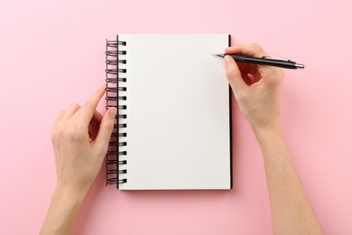 Photo of Woman writing in notebook on pink background, top view