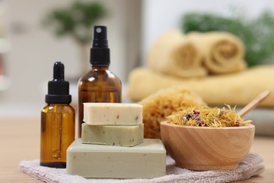 Photo of Bottles of essential oils, bowl with dry flowers, soap bars and natural sponge on light wooden table, closeup. Spa therapy