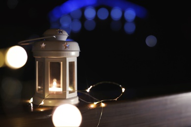 Photo of Lantern and Christmas lights on wooden railing outdoors against blurred background, space for text. Winter night