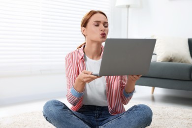 Photo of Woman sending air kiss during video chat via laptop at home. Long-distance relationship