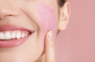Photo of Young woman applying natural scrub on her face against color background, closeup